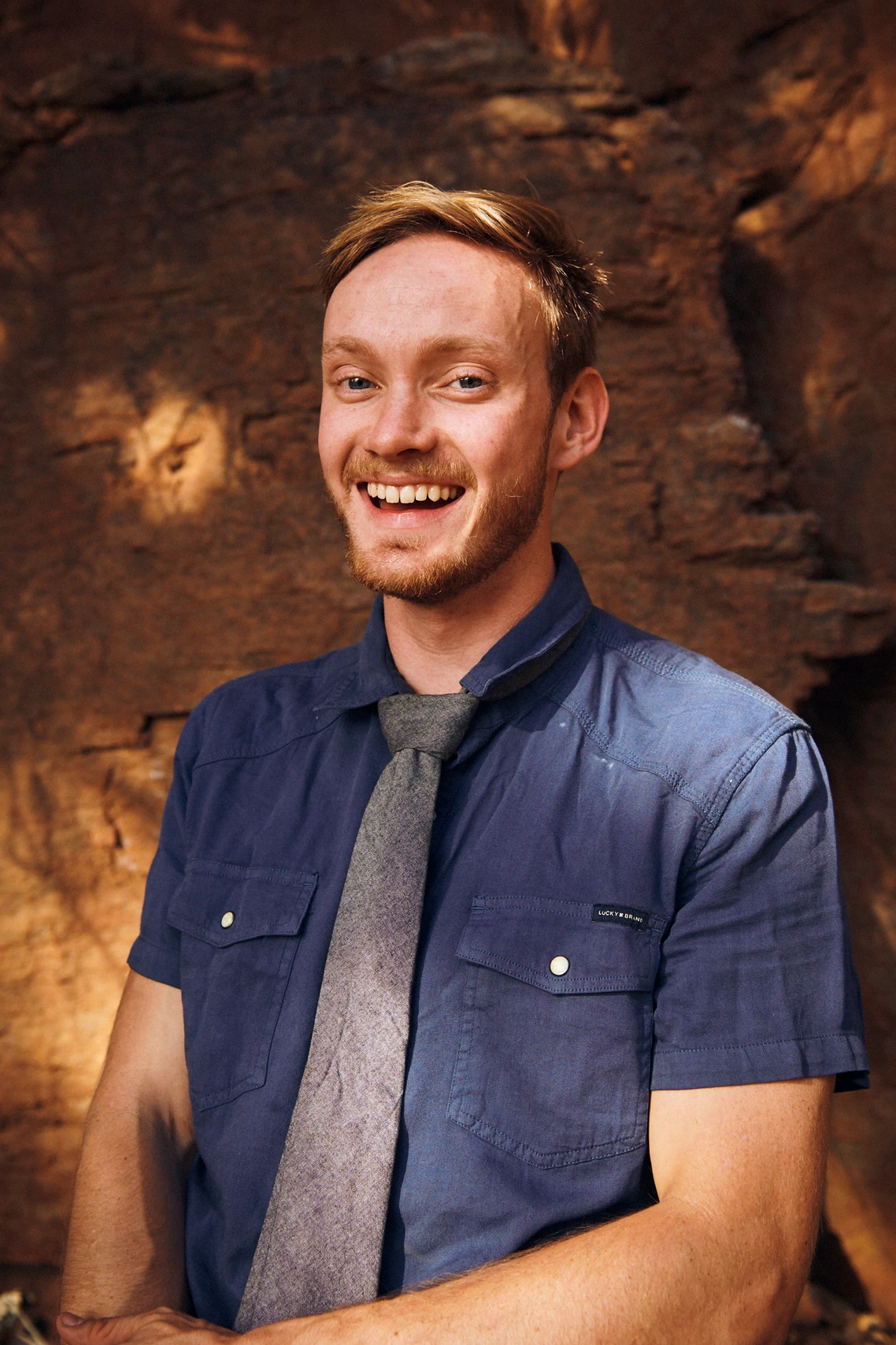 Devin Hunt smiling in a knit tie and short-sleeve shirt against a sandstone crag